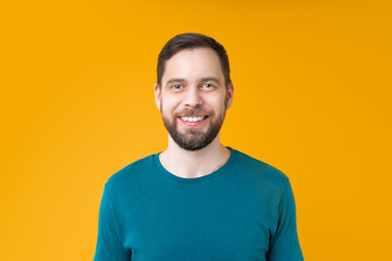 Close up studio portrait of young attractive bearded man smiling while standing over bright colored orange yellow background