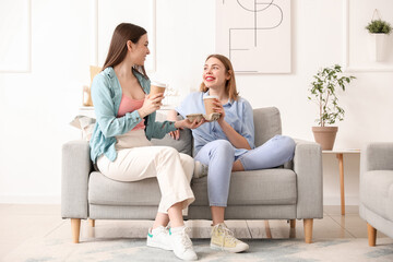 Female friends with cups of coffee sitting on sofa at home