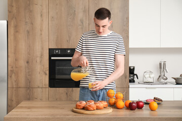 Young man pouring orange juice into glass in kitchen