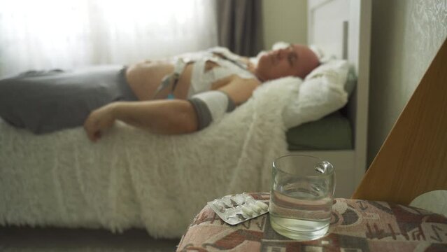 A man with a holter installed reveals malfunctions in the cardiovascular system. In the foreground in the zone of sharpness is a glass of water and medical capsules, in the background in a blurred bac