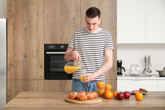 Young man pouring orange juice into glass in kitchen - Powered by Adobe