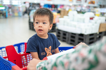 Multiracial toddler in shopping trolley in grocery store - 644187851