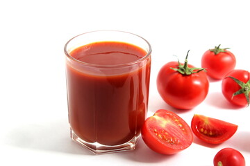 On a white background is a glass of tomato juice with tomatoes and herbs.