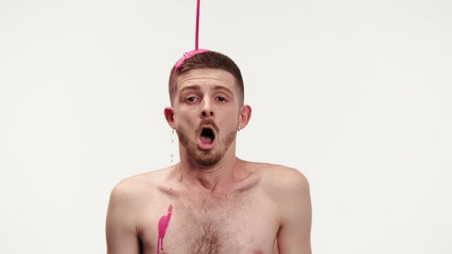 Young shirtless man being covered with thick pink paint against white studio background. Emotions. Abstract art on human body. Concept of creativity, inspiration