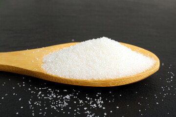 On a black background lies a wooden spoon with white crumbly sugar.