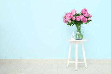 Vase of pink peonies with figurine on chair near blue wall