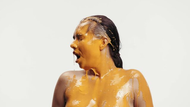 Young smiling woman with bare shoulders being covered with thick yellow paint against white studio background. Abstract art on human body. Concept of creativity, inspiration