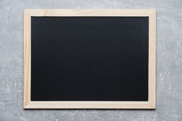 Black chalkboard for notes in wooden frame against gray concrete wall.