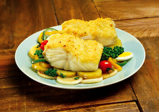 Prato com posta de bacalhau gratinado ao forno acompanhado de batata, cebola, brócolis e ovo cozido sobre mesa de madeira rústica - bacalhoada