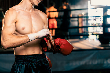 Determined Caucasian male boxer with muscularity physical readiness body wraps his hand and dons or wearing boxing glove, preparing for intense boxing training in the ring at gym. Impetus