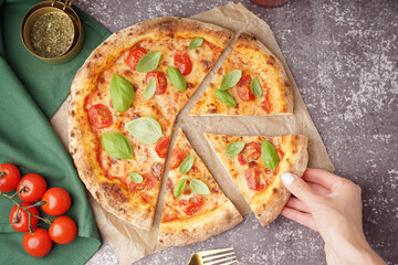 Woman taking piece of tasty pizza Margarita with tomatoes and basil on dark table