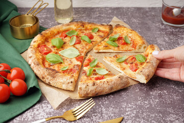 Woman taking piece of tasty pizza Margarita with tomatoes and basil on dark table