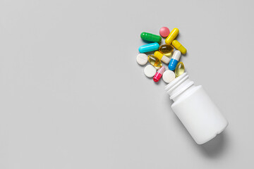 Jar with different scattered pills on grey background