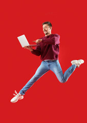 Jumping young man with laptop on red background