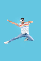 Fototapeta na wymiar Jumping young man with VR glasses on blue background