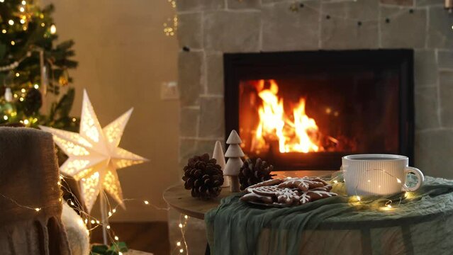 Cozy christmas. Gingerbread cookies and tea cup on table against festive christmas lights and burning fireplace. Winter hygge footage