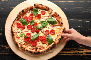 Woman taking slice of tasty pizza Margarita on black wooden background