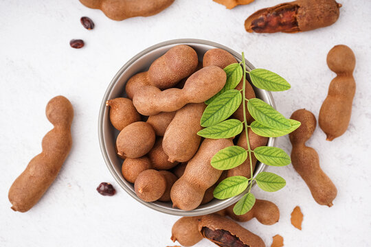 Bowl of tasty tamarinds and leaf on white background