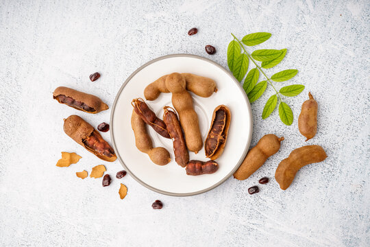 Plate of tasty tamarinds, seeds and leaf on white background