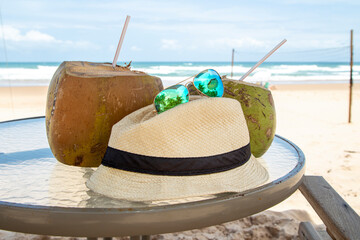 Chapéu de palha, óculos escuros, água de coco e praia do nordeste brasileiro