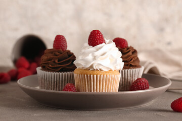 Plate of tasty cupcakes with raspberries on table
