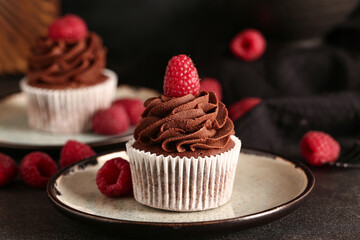 Plate of tasty chocolate cupcake with raspberries on black background