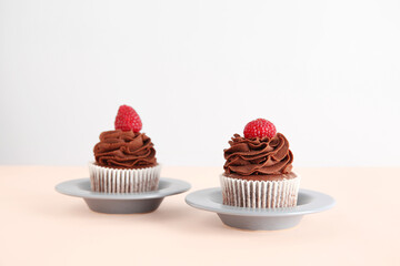 Plates of tasty chocolate cupcakes with raspberries on beige background