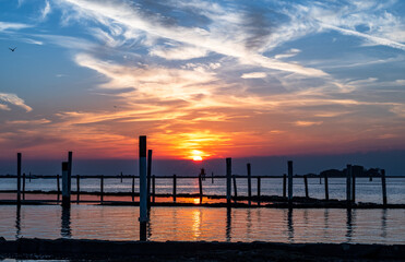 Fototapeta premium Sunset on the Grado Lagoon during a summer day. The sun is about to disappear over the horizon. Orange color and warm tones. A beautiful reflection on the sea. Taken near the Port.
