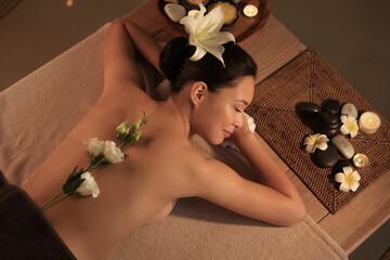 Young woman with flowers lying in dark spa salon, top view
