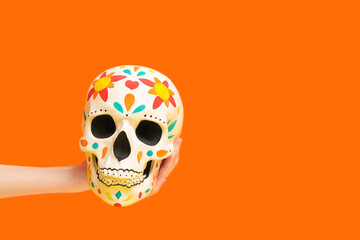 Female hand holding painted human skull for Mexico's Day of the Dead (El Dia de Muertos) on orange...
