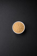 Raw ptitim pasta in a ceramic bowl on a dark concrete background