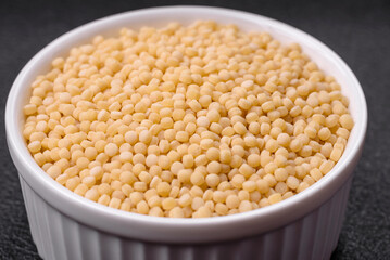 Raw ptitim pasta in a ceramic bowl on a dark concrete background