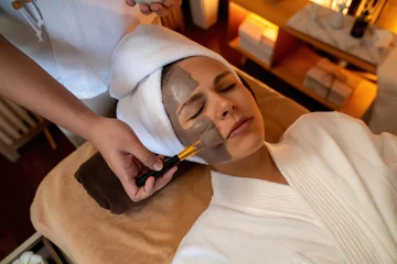 Foto auf Acrylglas Spa Serene ambiance of spa salon, woman customer indulges in rejuvenating with charcoal face cream massage with warm lighting candle. Facial skin treatment and beauty care concept. Quiescent