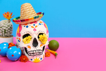 Mexican sugar skull with sombrero, flowers and lime on pink table against blue background. Mexico's...