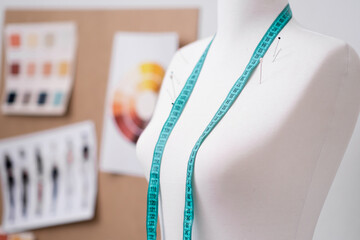 Green tape measure and pins on mannequin against board with swatches and sketches in fashion shop clothes sewing tools in contemporary atelier tailor studio closeup - obrazy, fototapety, plakaty