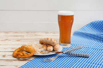 Plate with tasty Bavarian sausages, pretzel, sauerkraut and glass of beer on white wooden background. Oktoberfest celebration