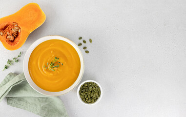 Pumpkin soup with creamy texture and pumpkin seeds on a gray background. Top view, copy space.