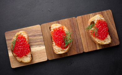 Red caviar on slices of white wheat bread on a black table, concept of luxury and gourmet cuisine