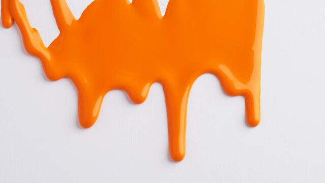 Liquid drops of orange paint color flowing on the white surface. Macro shot of orange paint dripping on the white canvas with copy space. Abstract art.