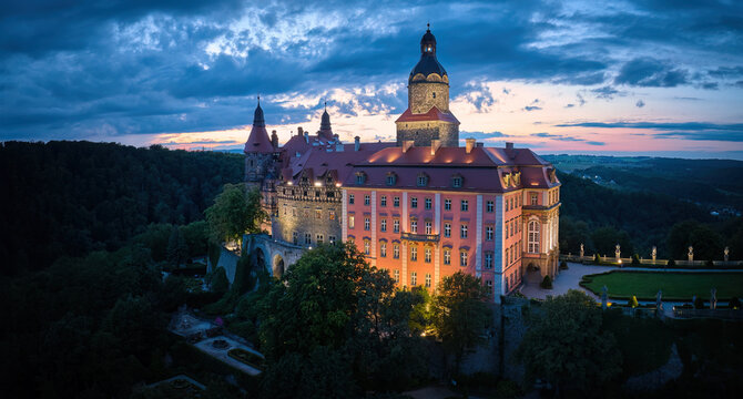 Evening, panoramic aerial view of the illuminated Ksiaz Castle, Schloss Fürstenstein, a beautiful castle standing on a rock surrounded by the forest of Lower Silesian Voivodeship, Poland.