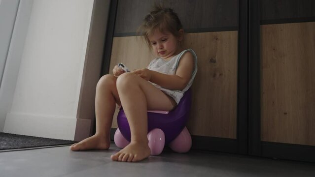 Toddler baby girl going to the toilet sitting on the potty, indoors in the living room. Baby learning to go to the toilet on lifestyle potty.
