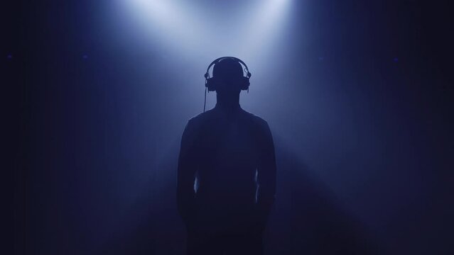Backlit silhouette of dj man, saxophonist, singer vocalist woman standing in dark nightclub disco studio and start performance. Blue light appears and illuminates each person of musician group band