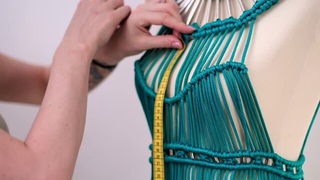 Designer creates unique green macrame dress on dummy in sewing atelier blonde woman ties knot on unfinished garment made of threads in dressmaking workshop