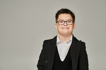 carefree schoolboy with down syndrome and genuine smile looking at camera on grey,  portrait