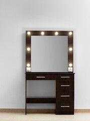 Modern dark makeup dressing table with mirror and backlight against a white wall.