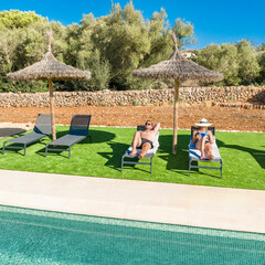Couple relaxing on loungers under a parasol by the swimming pool -