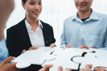 Diverse corporate officer workers collaborate in office, connecting puzzle pieces to represent...