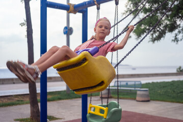 A delighted girl in pink dress swings, thoroughly enjoying herself at the urban park's playground. 