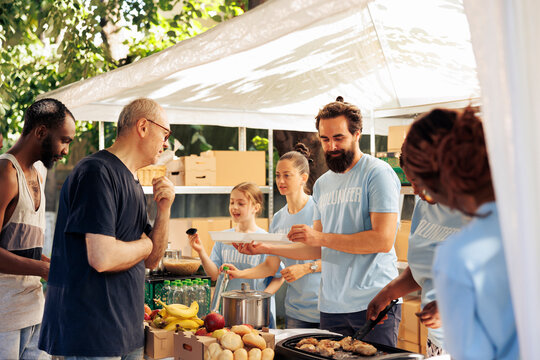 Members of diverse charity group provide assistance and distribute food donations to the homeless and less fortunate at the shelter. Volunteers at food drive handing out warm meals to poor people.