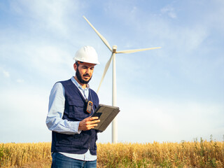 Male engineer examines with a tablet in a field of wind mills. Electricity Creation Station